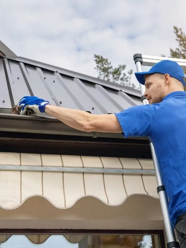 A technician cleaning gutters on a residential home to prevent water damage.