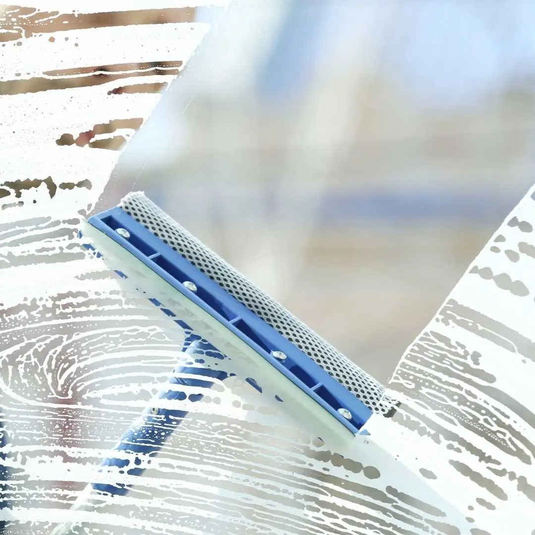 Professional window cleaner working on residential windows using proper tools for streak-free results.