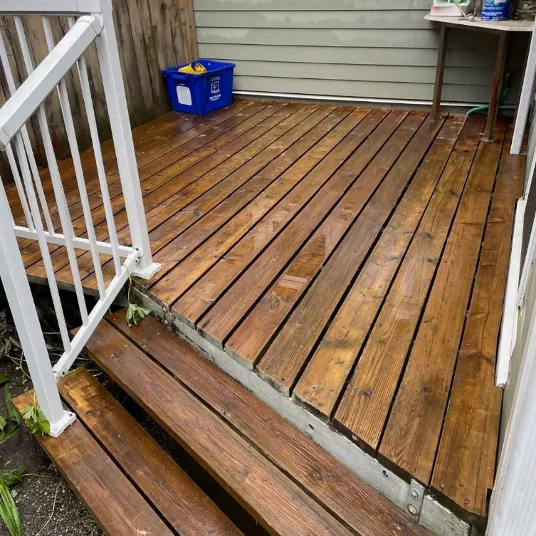 Wet wooden deck with stairs and railing, showing moisture on the surface after recent rain.