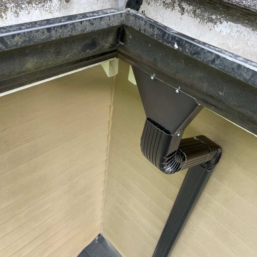 Corner gutter system with newly installed downspout on a residential roof, ready for proper rainwater drainage.