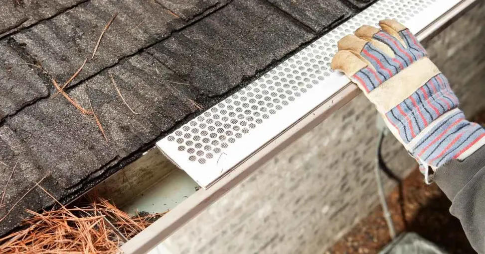 Installing gutter guard on roof with leaves.